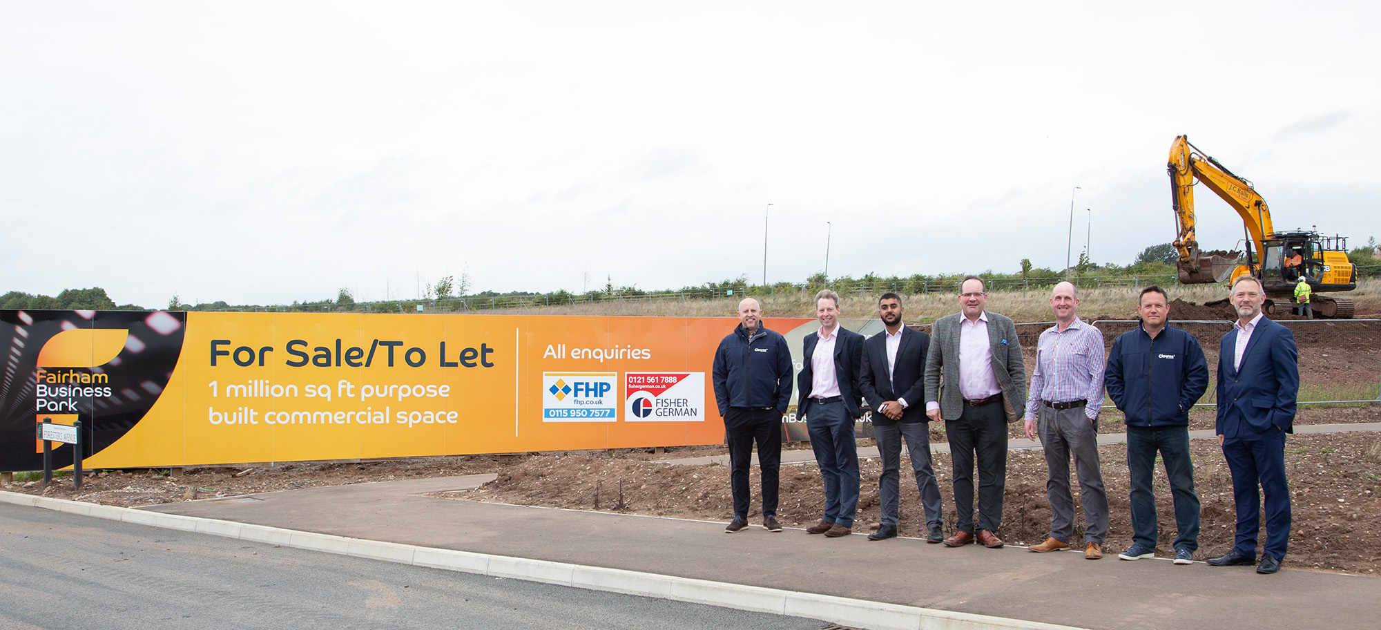 Fairham Business Park. 7 men stood by Fairham Business Park branded hoarding and a digger in the background