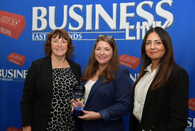 Business Link awards. Three women, one holding an award in front of a blue photo back drop