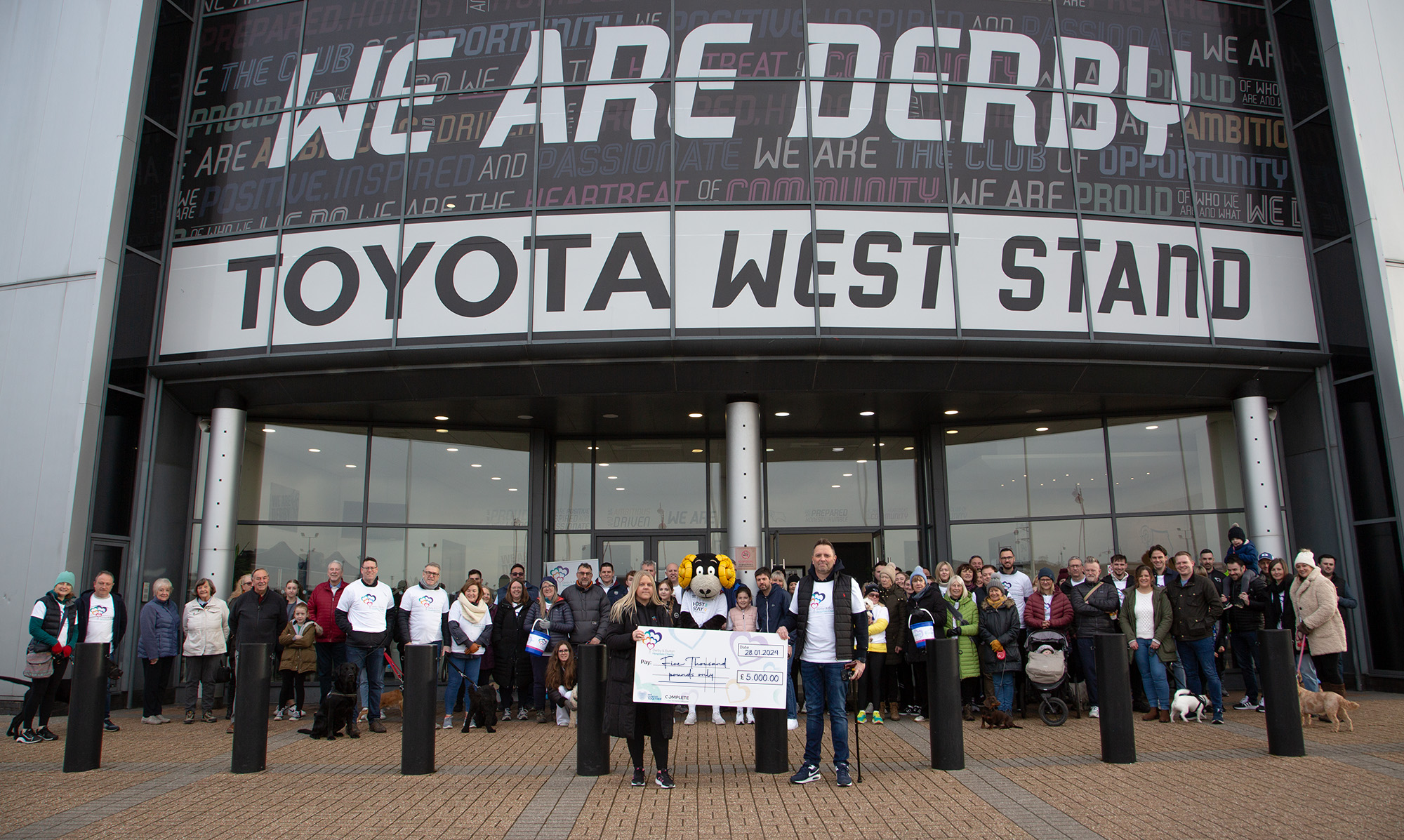 Group of people stood in front of Derby County Football stadium holding a cheque.