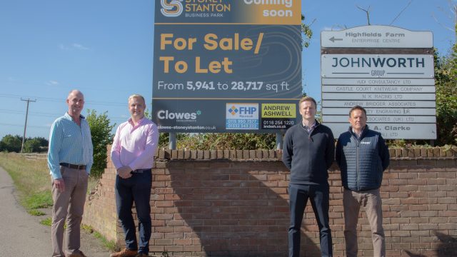 four men stood in front of a brick wall with a sign above them