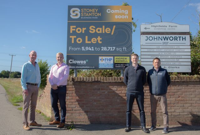 four men stood in front of a brick wall with a sign above them