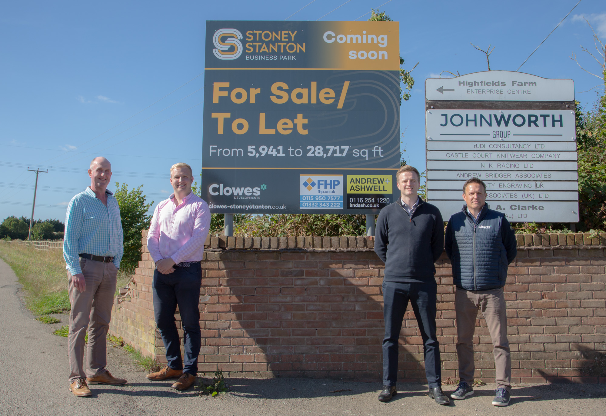 four men stood in front of a brick wall with a sign above them